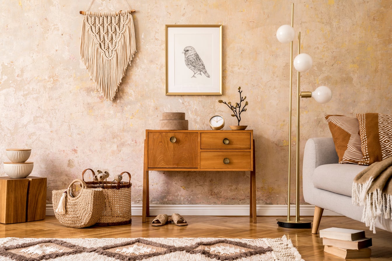 Modern retro composition of living room with wooden vintage commode, grey sofa, gold lamp, macrame, carpet, pillows, gold mock up poster frame, plants, decoration and personal accessories.